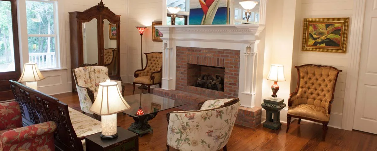 Living room with a brick fireplace, white mantel, wood floors and upholstered chairs