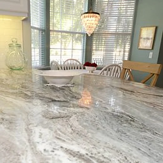 Close-up of a polished granite countertop in a kitchen with a dining table and window light