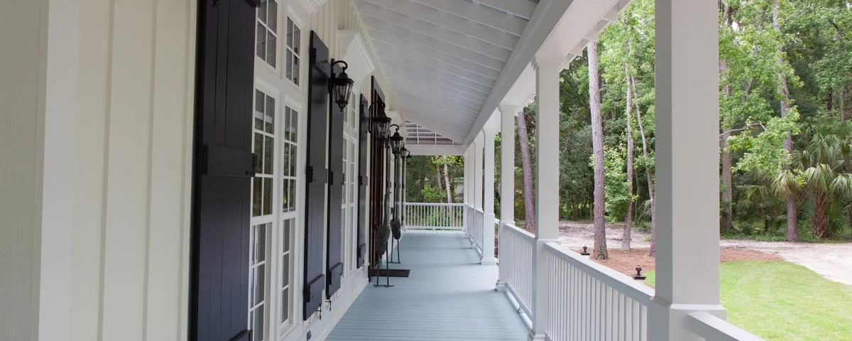 Long white porch with square columns, black shutters, lanterns and a painted wood ceiling